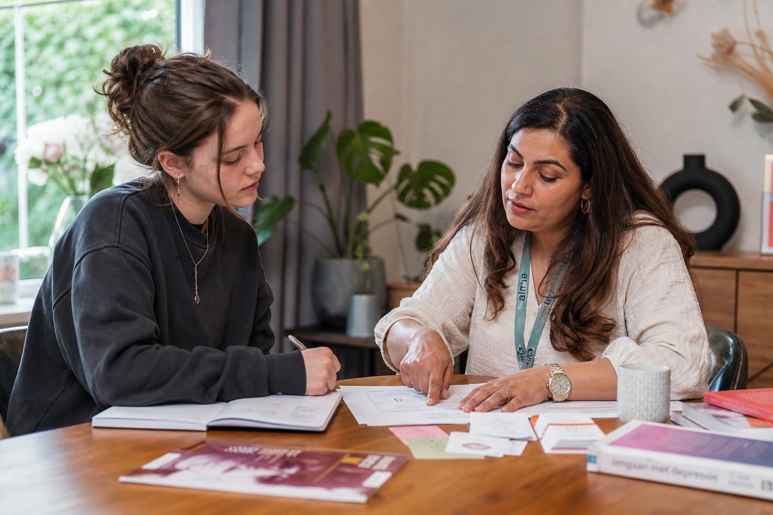 Ambulant begeleider en jongvolwassene samen aan een tafel met psycho-educatie materiaal in een huiselijke omgeving